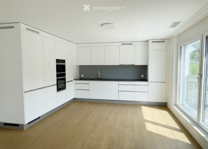 Modern, minimalist kitchen with white cabinets, a dark grey backsplash, and a light wooden floor. Features include a built-in oven and a sink with a modern faucet.
