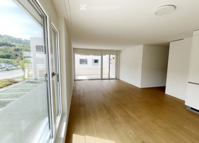 Empty room with light wooden flooring, white walls, large windows, and a sliding glass door leading to an outdoor area.