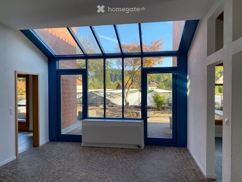 Bright, modern hallway with large glass windows and doors, brick flooring, and white walls.