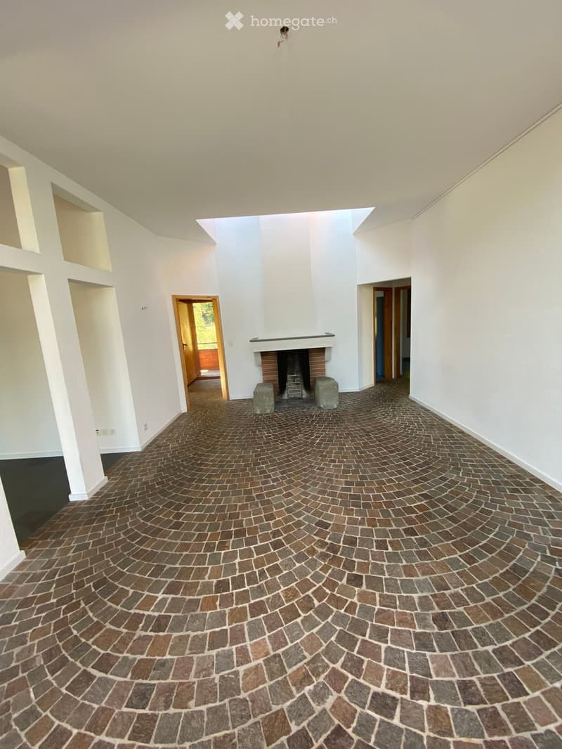 Spacious hallway with a curved brick floor, white walls, and a central fireplace with a brick surround and two stone stools on either side.