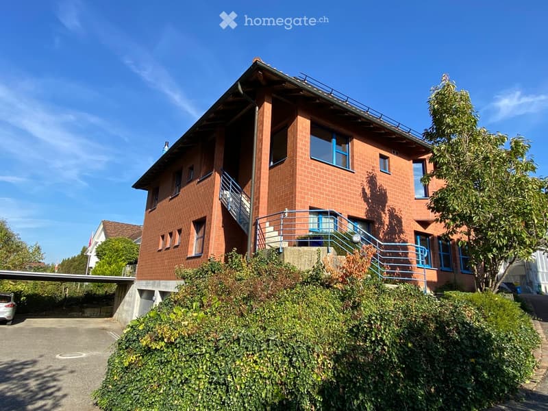Two-story brick house with blue-framed windows, a raised ground floor, and a staircase leading to a balcony.