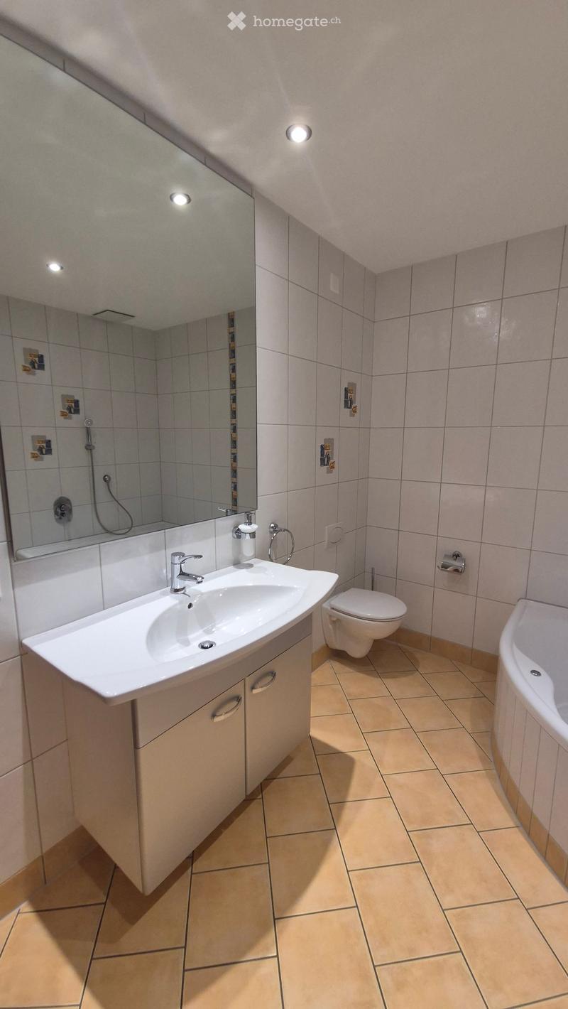 Modern bathroom with a white sink, toilet, bathtub, and large mirror. Light-colored tiles and a sleek design.