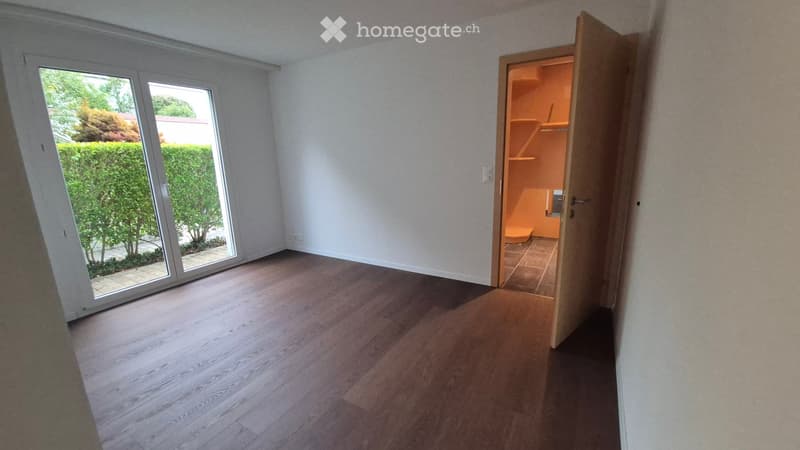 Empty room with wooden flooring, white walls, large sliding glass door leading to a garden, and an open closet with shelves.