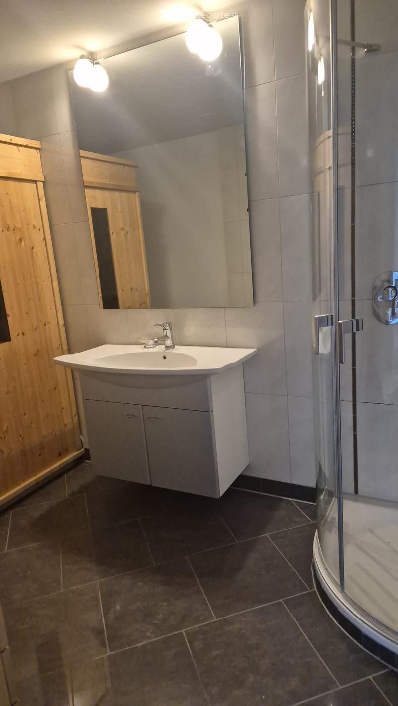 Modern bathroom with a white sink, mirrored cabinet, and a glass-enclosed shower. Dark tiled floor and walls.
