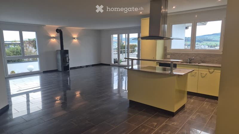 Modern kitchen with a central island, light yellow cabinets, dark tiled floor, and large windows offering a scenic view.