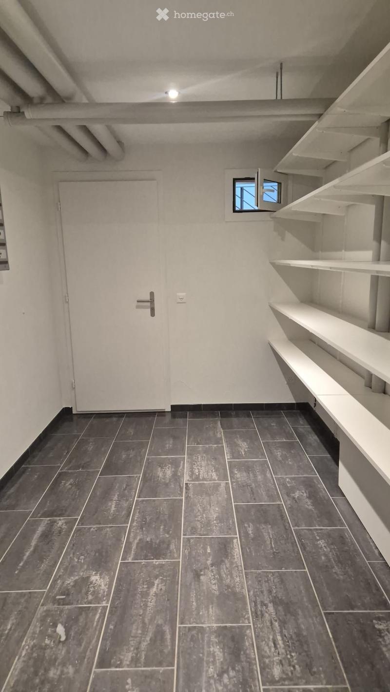 Empty hallway with grey tiled floor, white walls, a closed door, and built-in white shelving unit on one side.