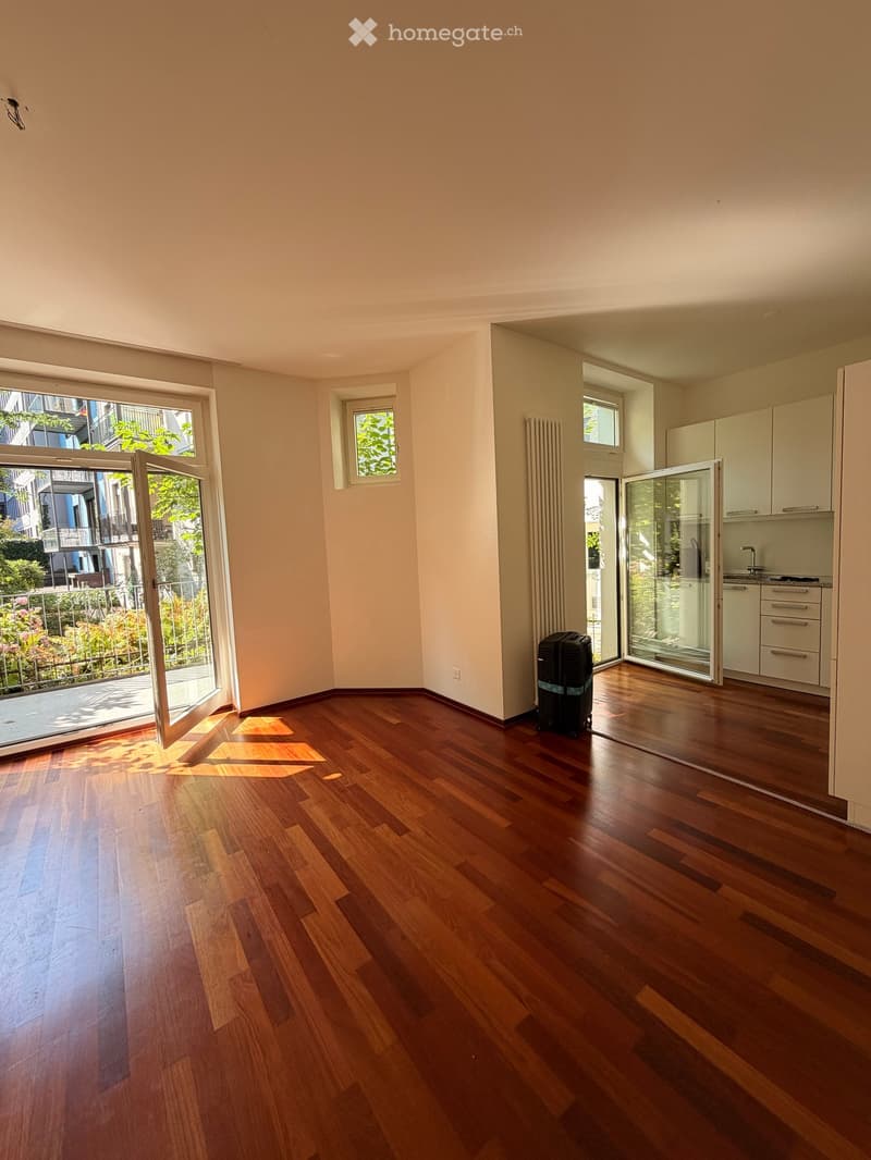 Empty room with wooden flooring, large windows, and a view of a balcony area with greenery.