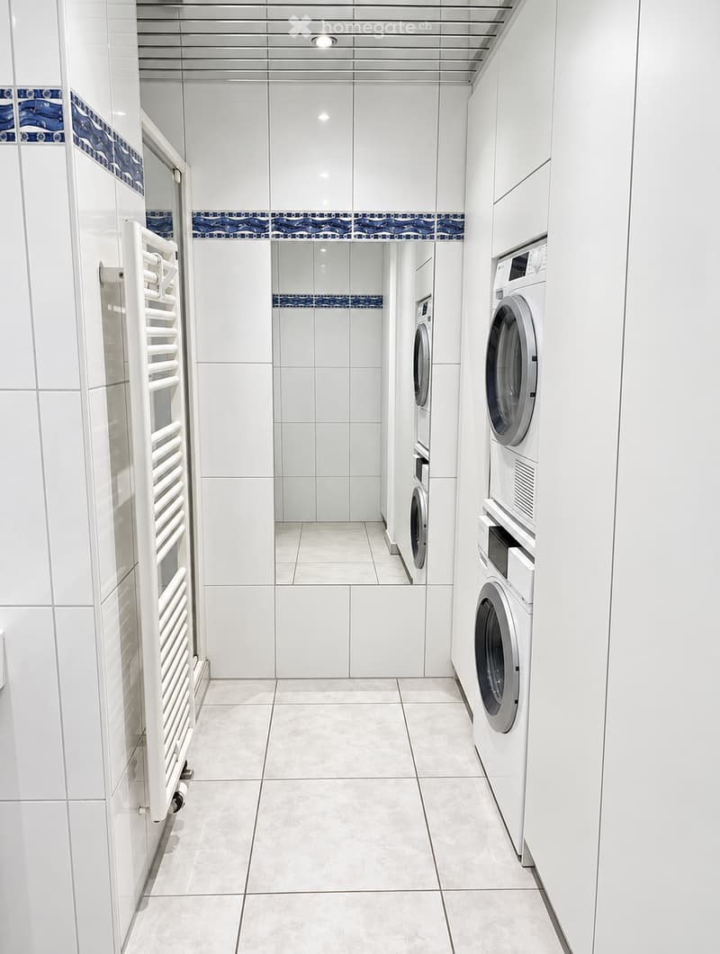Clean, modern laundry room with white tiled walls, a washing machine, dryer, and a towel rack.