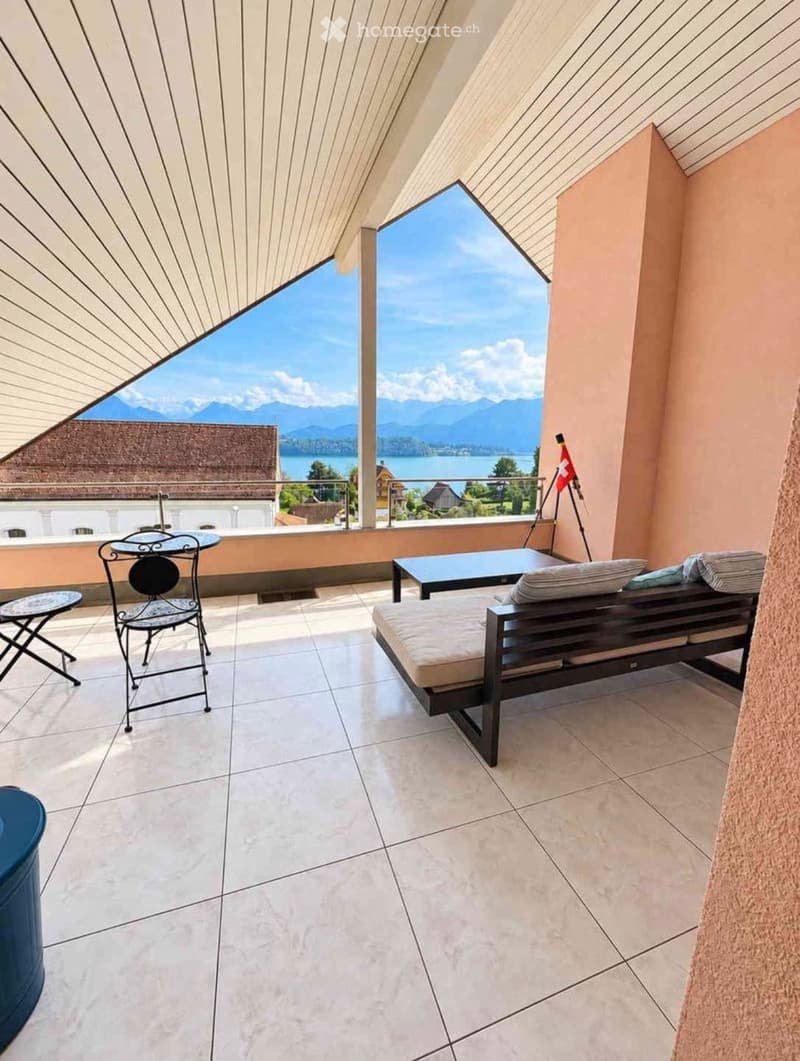 Balcony with tiled floor, daybed, small table and chairs, scenic mountain and lake view.
