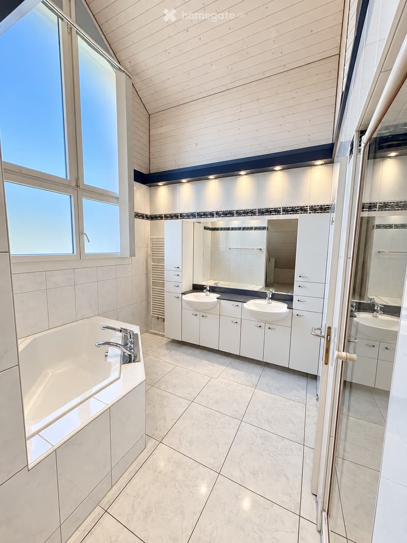Modern bathroom with a large bathtub, double sink vanity, mirrored cabinets, and large windows providing natural light.