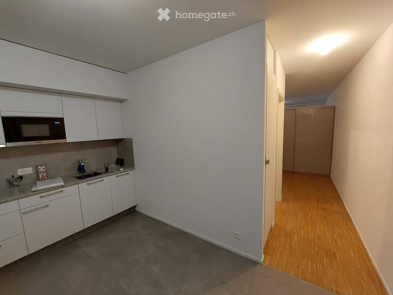 A modern kitchen with white cabinets, a microwave, a sink, and a small hallway leading to another room.