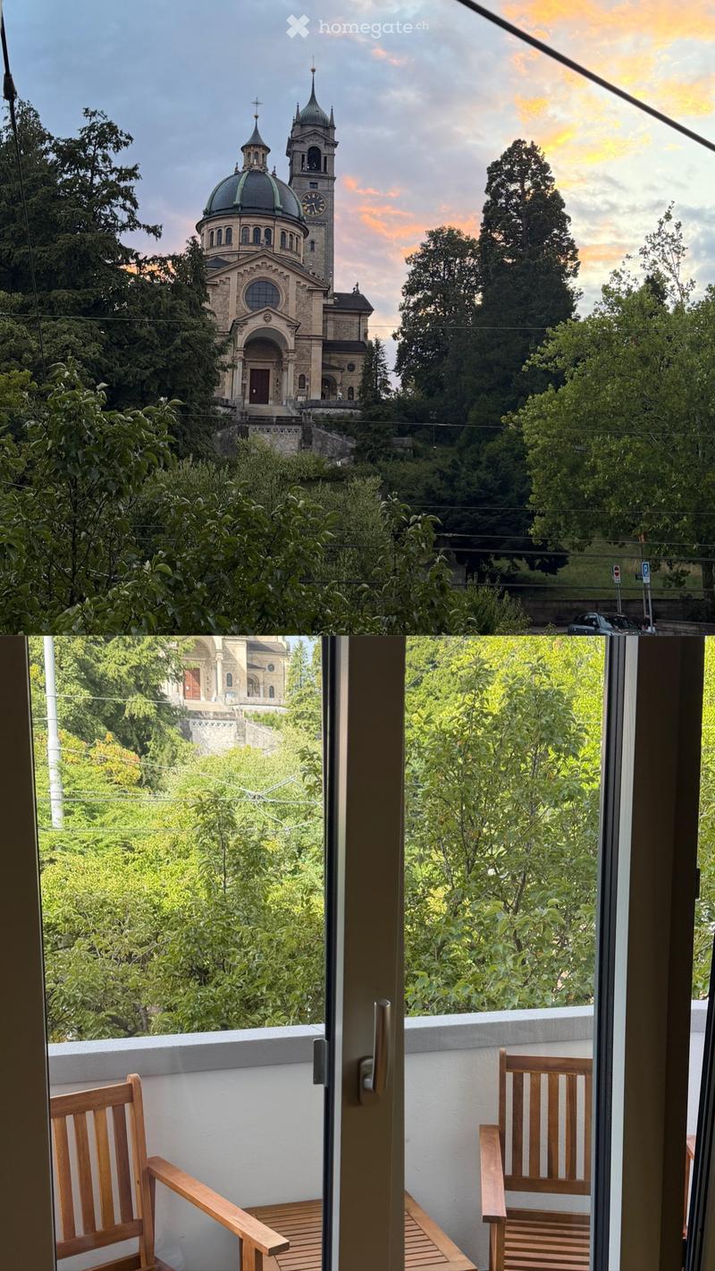 Balcony with wooden chairs, overlooking a lush green area and a historic church with a dome and tower.
