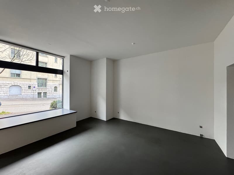 Empty room with white walls, dark floor, and large window showing an urban view.