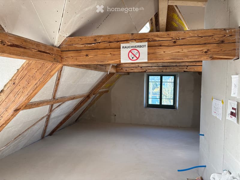Empty attic space with exposed wooden beams, a single window, and a no-smoking sign on the ceiling beam.