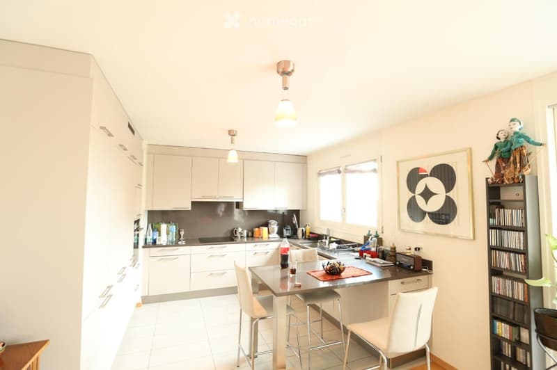 Modern kitchen with white cabinets, stainless steel appliances, a central island with a dining table and chairs, and a large window providing natural light.