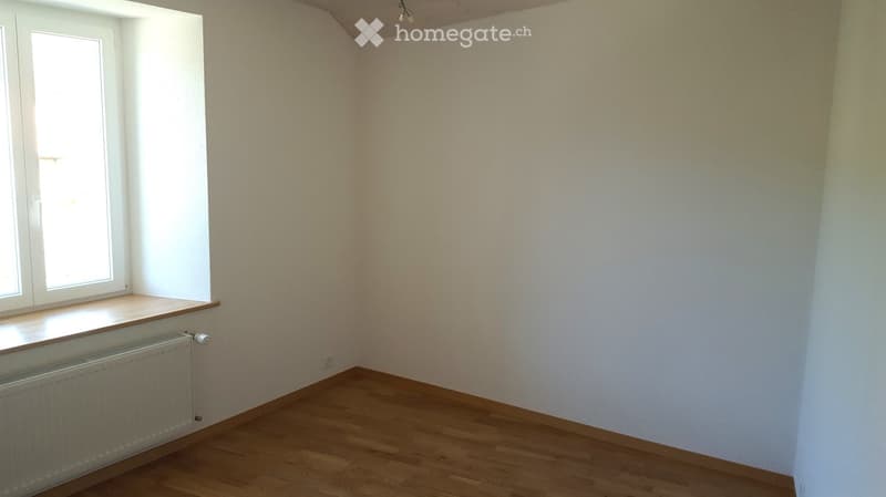Empty room with wooden flooring, white walls, and a window with a radiator below it.