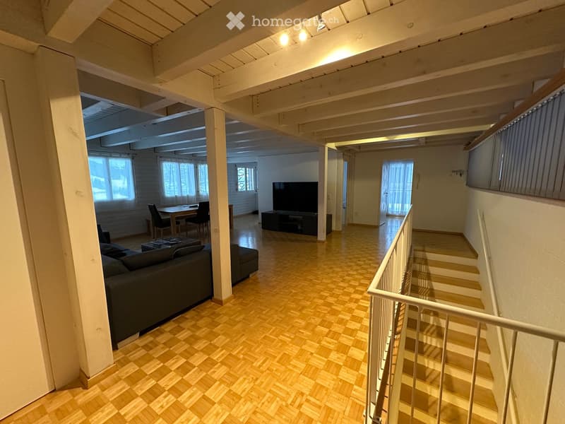 Open-plan living and dining area with wooden flooring, a staircase leading to another level, and modern furnishings including a sofa, coffee table, TV, and dining set.