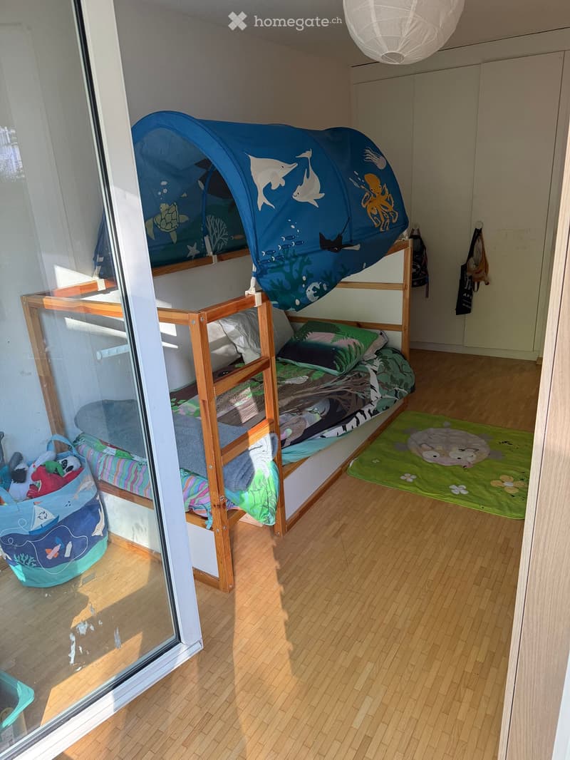 Cozy children's bedroom with a bunk bed, a colorful toy tent, a green rug, and a toy bag on the floor.