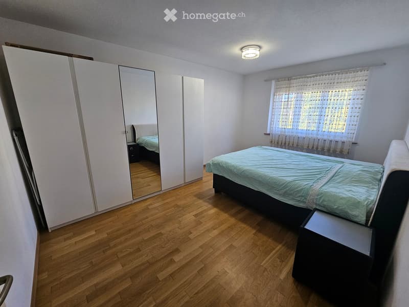 Bedroom with wooden flooring, a bed with blue bedding, a large mirrored wardrobe, and a nightstand.
