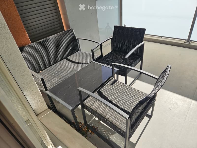 Balcony with a wicker sofa, two wicker chairs, and a glass table, overlooking a scenic view.