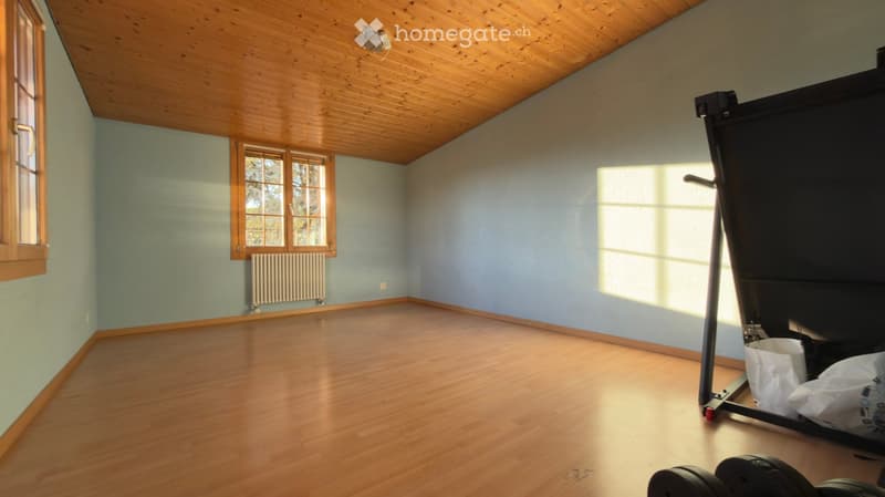 Empty room with wooden flooring, light blue walls, and wooden-framed windows. The room is completely unfurnished, with no visible furniture or equipment.
