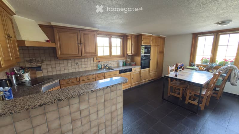 Bright kitchen with wooden cabinets, granite countertops, and a central island. Includes a sink, oven, dishwasher, and a dining area with a table and chairs.