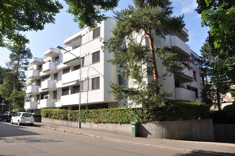 white building, multiple balconies, street lamp, hedge, cars parked