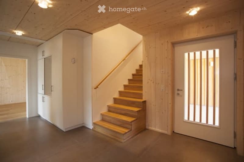 Bright, modern hallway with wooden staircase, white walls, and recessed lighting. Features a built-in cabinet and a frosted glass door leading to another room.