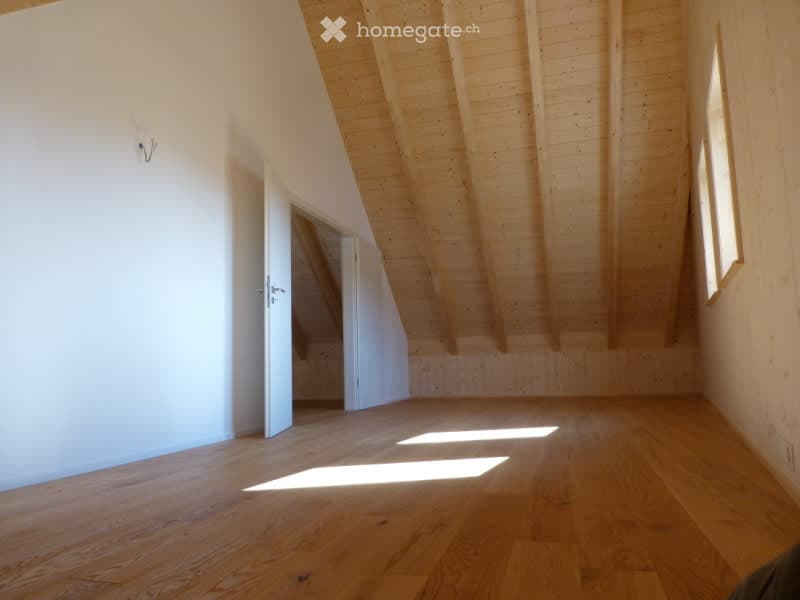 Empty attic room with wooden beams, wooden floor, and natural light from windows. No furniture or equipment present.