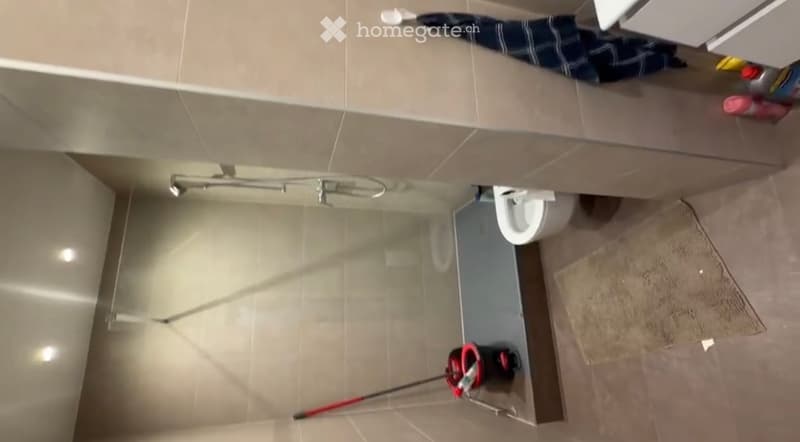 Modern bathroom with a toilet, shower, and a bathroom cabinet. A towel is draped over the cabinet, and a mop is placed on the floor.