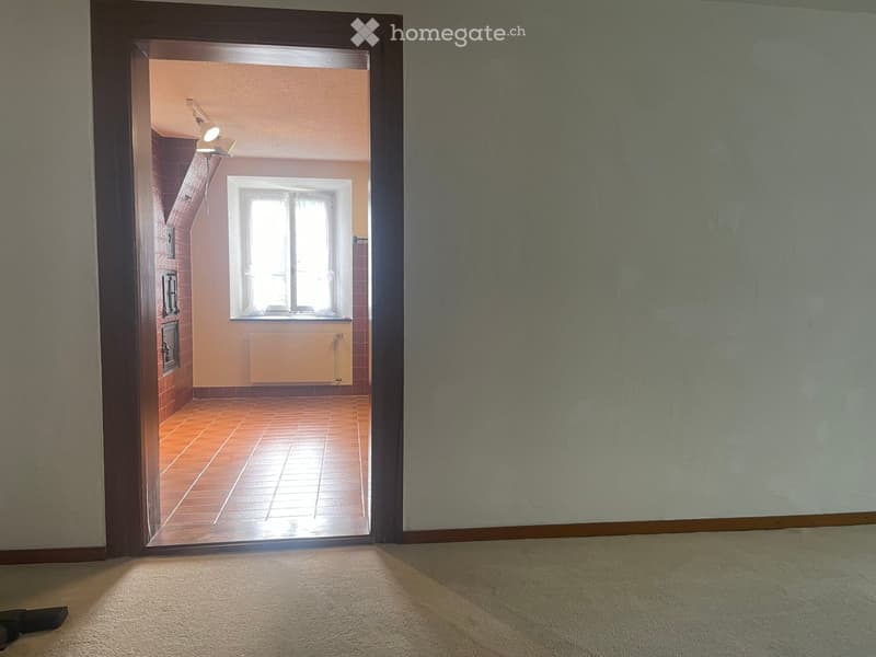Empty room with carpeted floor and open doorway leading to another room with tiled floor, window, and radiator.