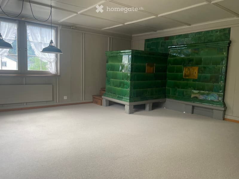 Empty room with carpeted floor, green tiled fireplace, large windows with white curtains, and pendant lights.