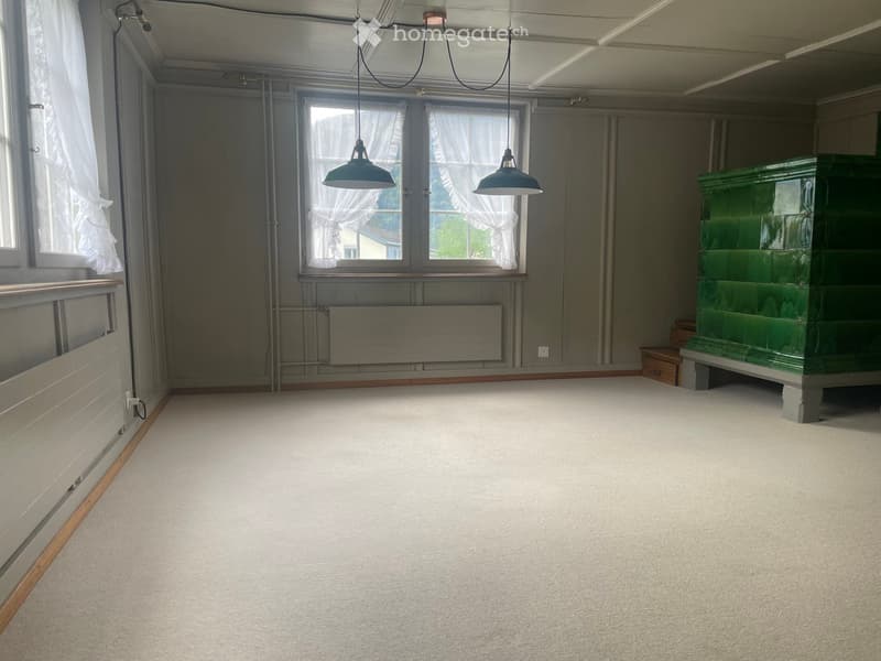 Empty room with light grey walls, carpeted floor, large windows with white curtains, and a green antique cabinet in the corner.