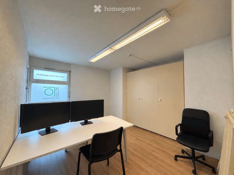Modern office space with a white desk, two computer screens, two black office chairs, and a built-in cabinet.
