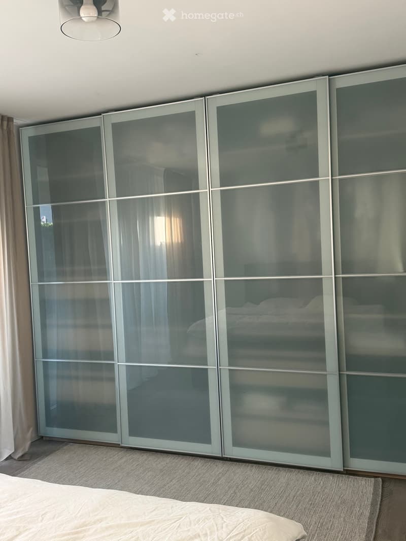 Modern bedroom with a large sliding wardrobe and a neatly made bed.