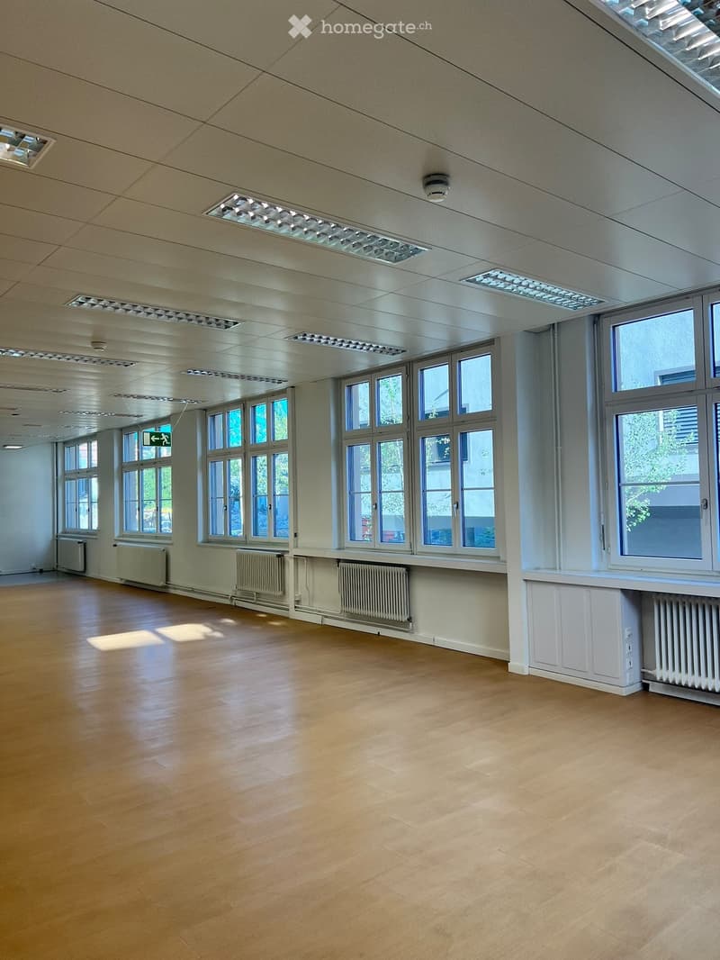Empty room with wooden flooring, large windows, radiators, and recessed ceiling lighting.