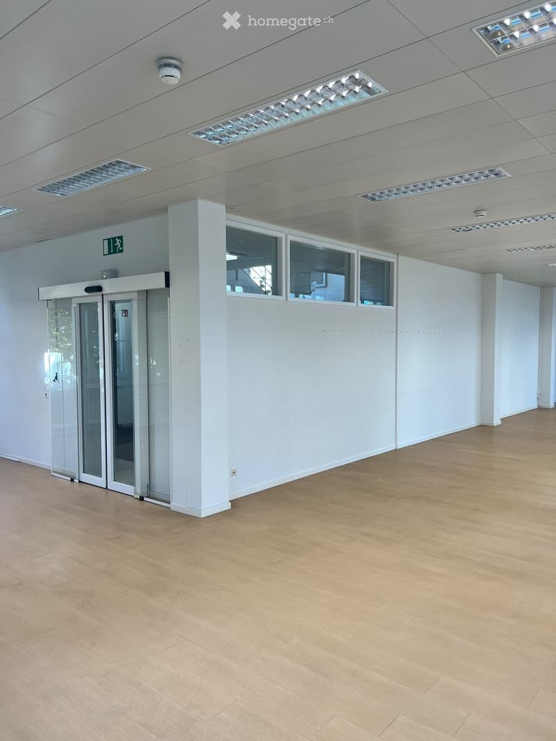 Empty room with light wooden flooring, white walls, and a glass door leading outside. The ceiling features recessed lighting and air vents.