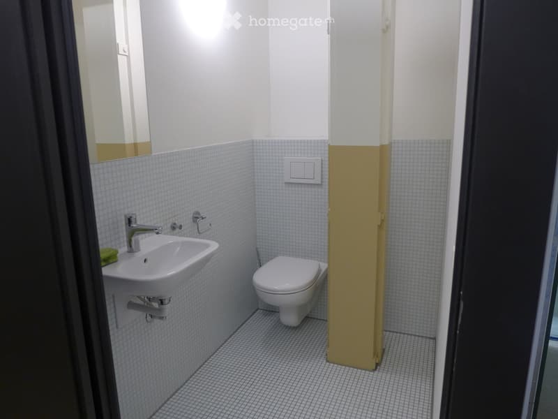 Compact bathroom with white tiled walls and floor, featuring a sink with a modern faucet, a toilet, and a mirror above the sink.