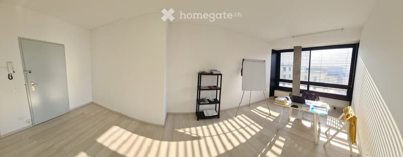 Empty room with white walls, wooden floor, a door, a bookshelf, a whiteboard on a stand, a desk, and windows with blinds.