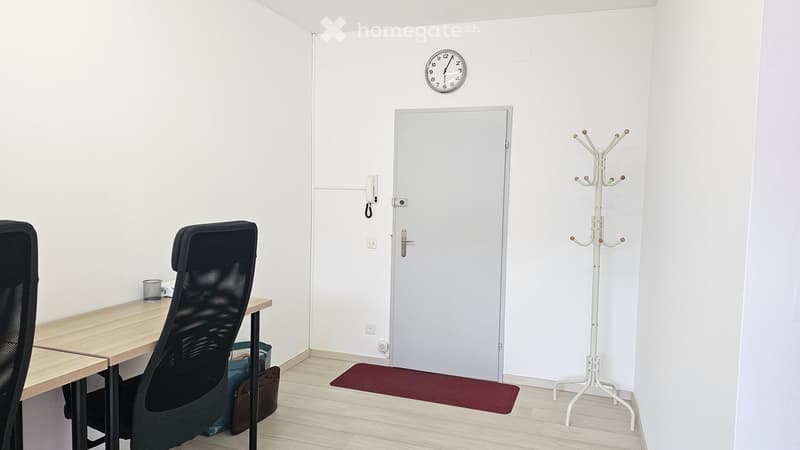 Modern office room with wooden desk, black office chairs, rug in front of the door, coat rack, clock, telephone on the wall