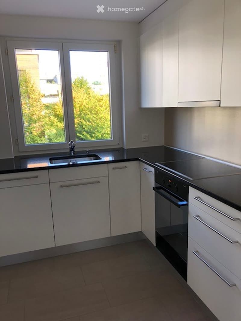 Modern kitchen with white cabinets, black countertops, a sink, and an oven. Large windows provide natural light.