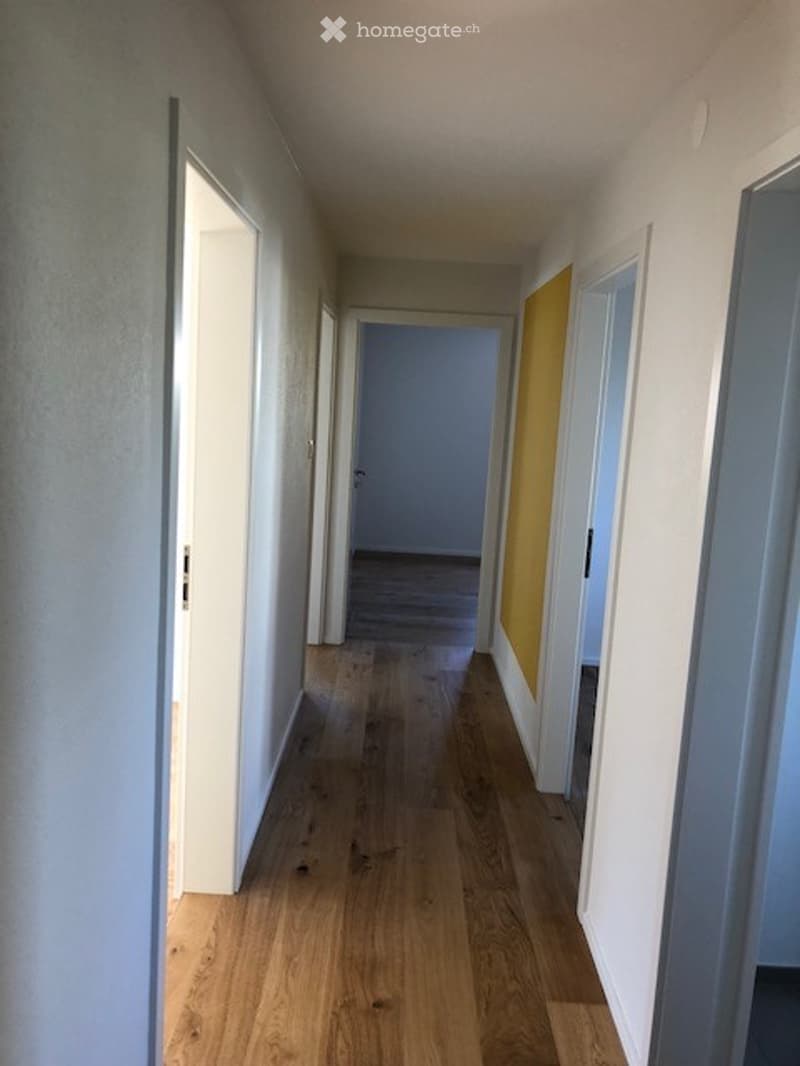 Empty hallway with wooden flooring, white walls, and several open doors leading to other rooms.