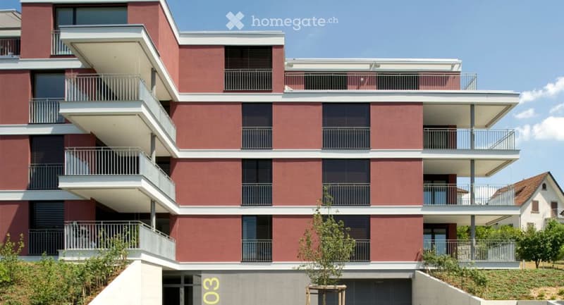 Modern multi-story apartment building with red brick facade, white trim, and multiple balconies.