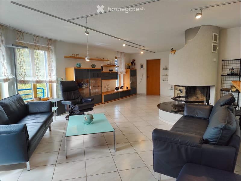 Modern living room with a black leather sofa, glass coffee table, armchair, fireplace, and built-in cabinetry with glass shelves.