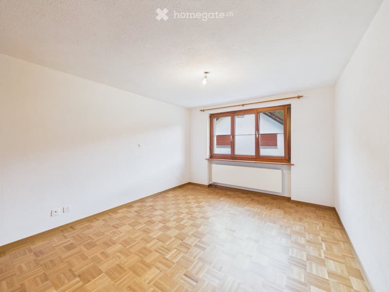 Empty room with wooden flooring, white walls, and a large window with wooden frame and radiator below.