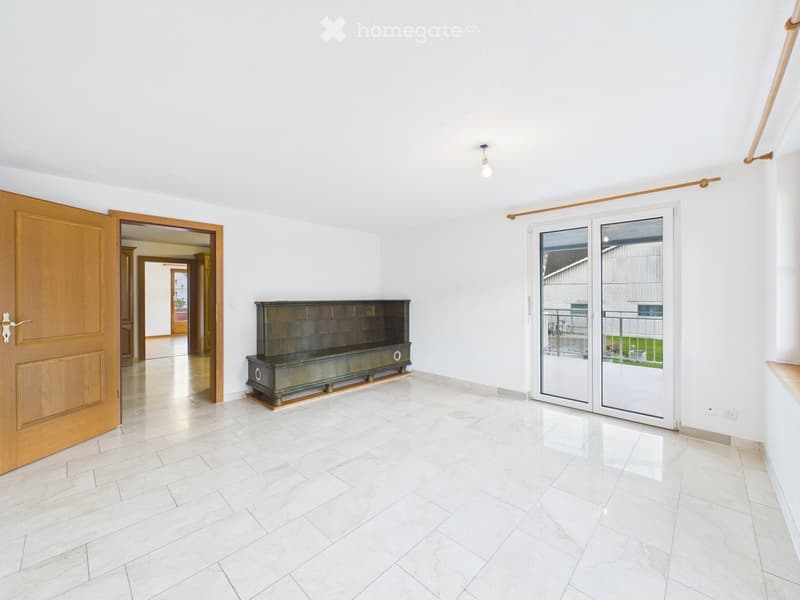 Bright hallway with white walls, tiled floor, wooden doors, and a small bench near a sliding glass door leading to an outdoor area.
