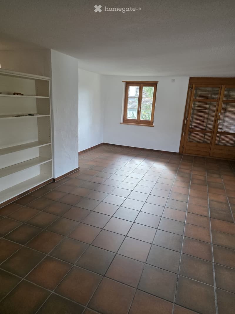 Empty room with tiled floor, white walls, a window with wooden frame, and a wooden door with blinds.