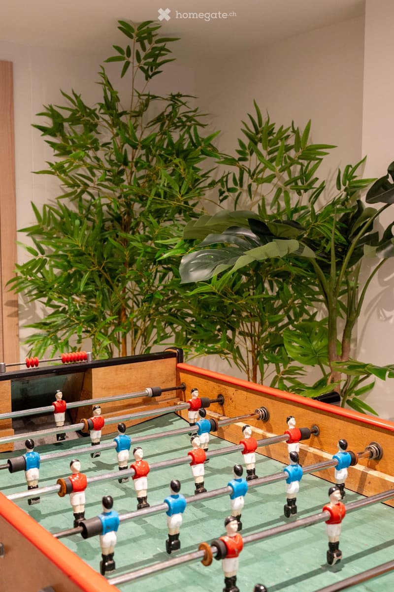 A small room with a foosball table and several potted plants in the background.