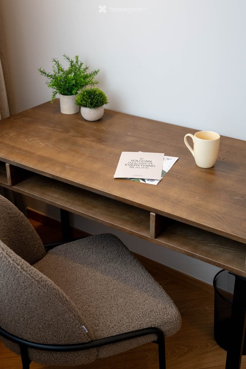 A modern, minimalist room with a wooden table, a comfortable chair, a cup, potted plants, and a magazine on the table.