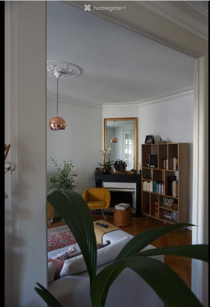 Living room with a white sofa, coffee table, yellow armchair, bookshelf, mirror, piano, and decorative plants.